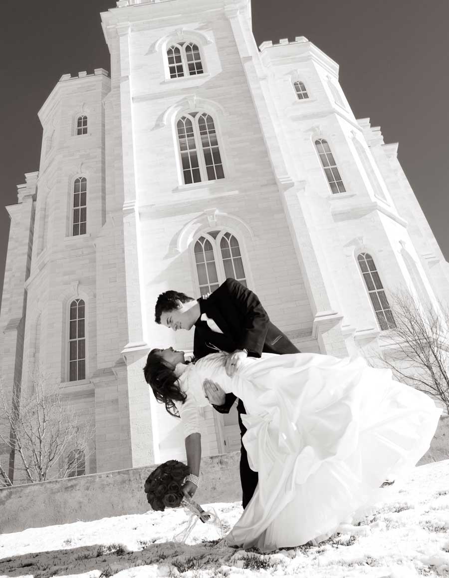 Bride and groom in a dip pose on snowy ground in front of the Manti Temple, in black and white